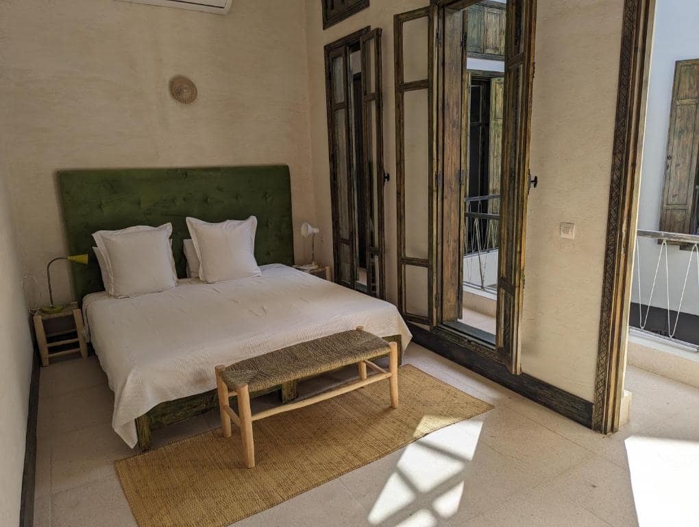 Une chambre à tête de lit verte, volets de cèdre ouverts sur le derb
