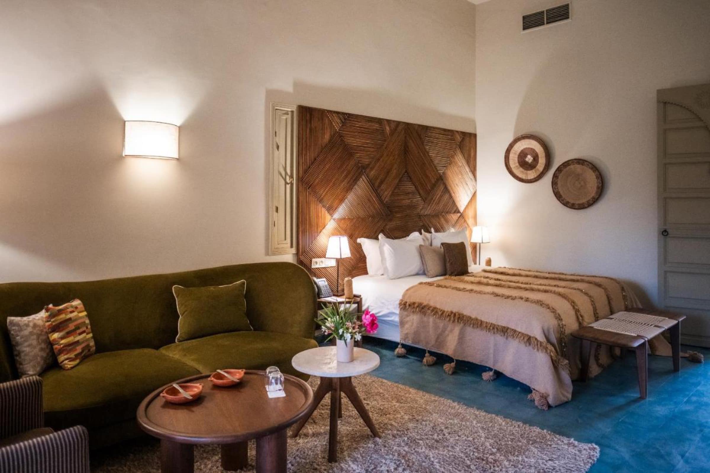 Une chambre à tête de lit tressée, canapé vert et tomettes