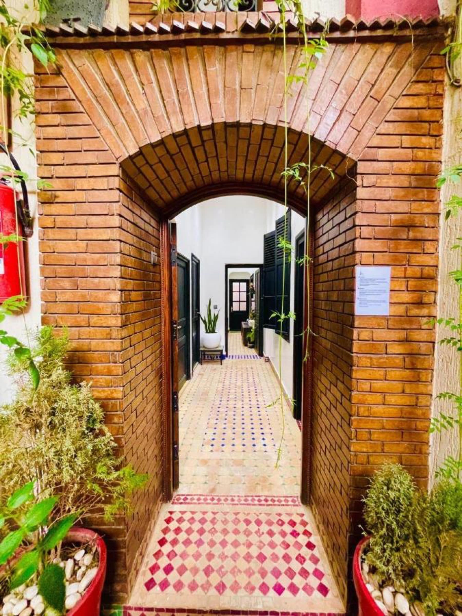 L'entrée sous une arche de brique, chemin de zellige