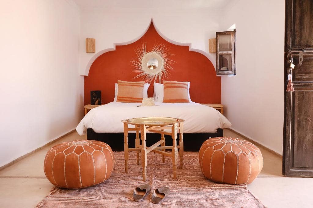 Une chambre, tête de lit ocre rosé et poufs de cuir