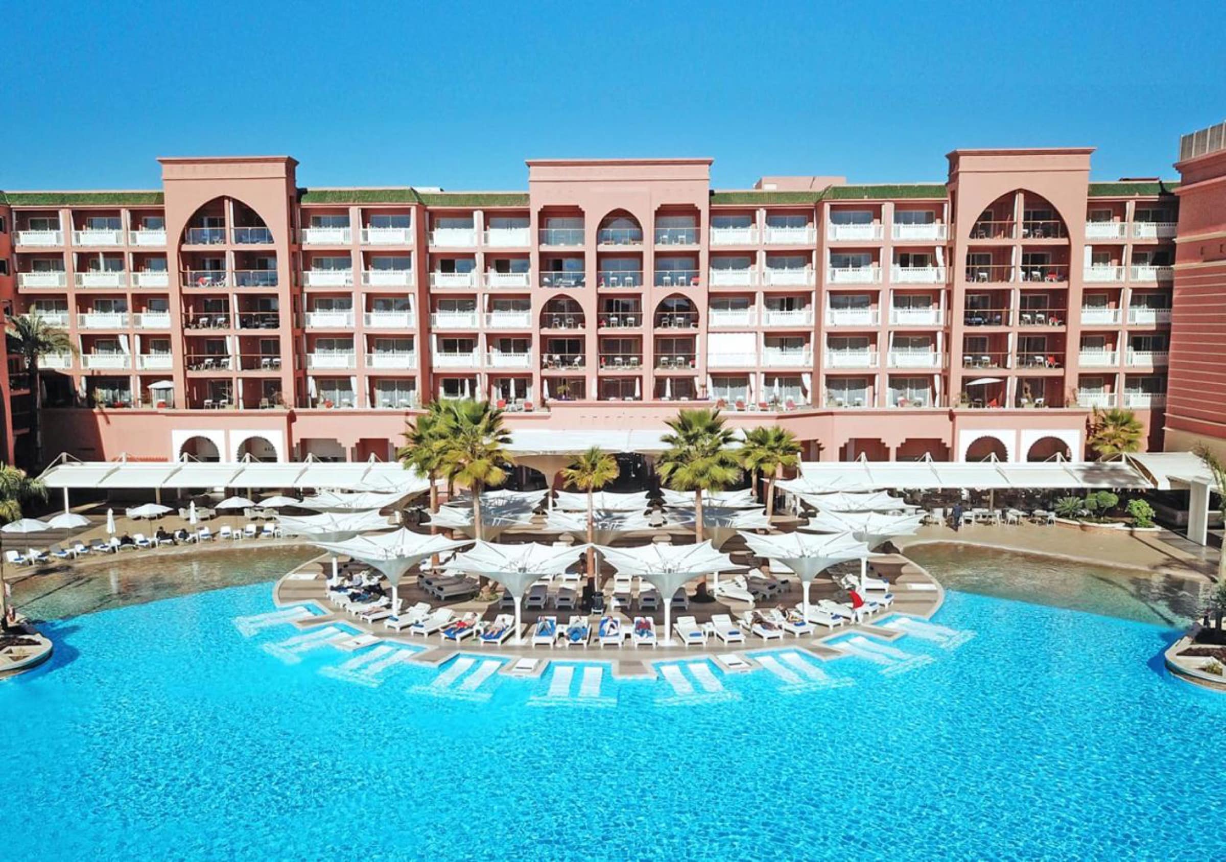 La façade rose et la grande piscine à parasols, vue du ciel
